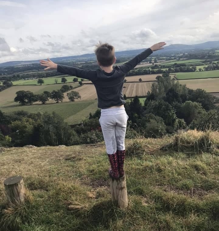 Callum standing on a Shropshire hilltop with arms outstretched, overlooking the countryside